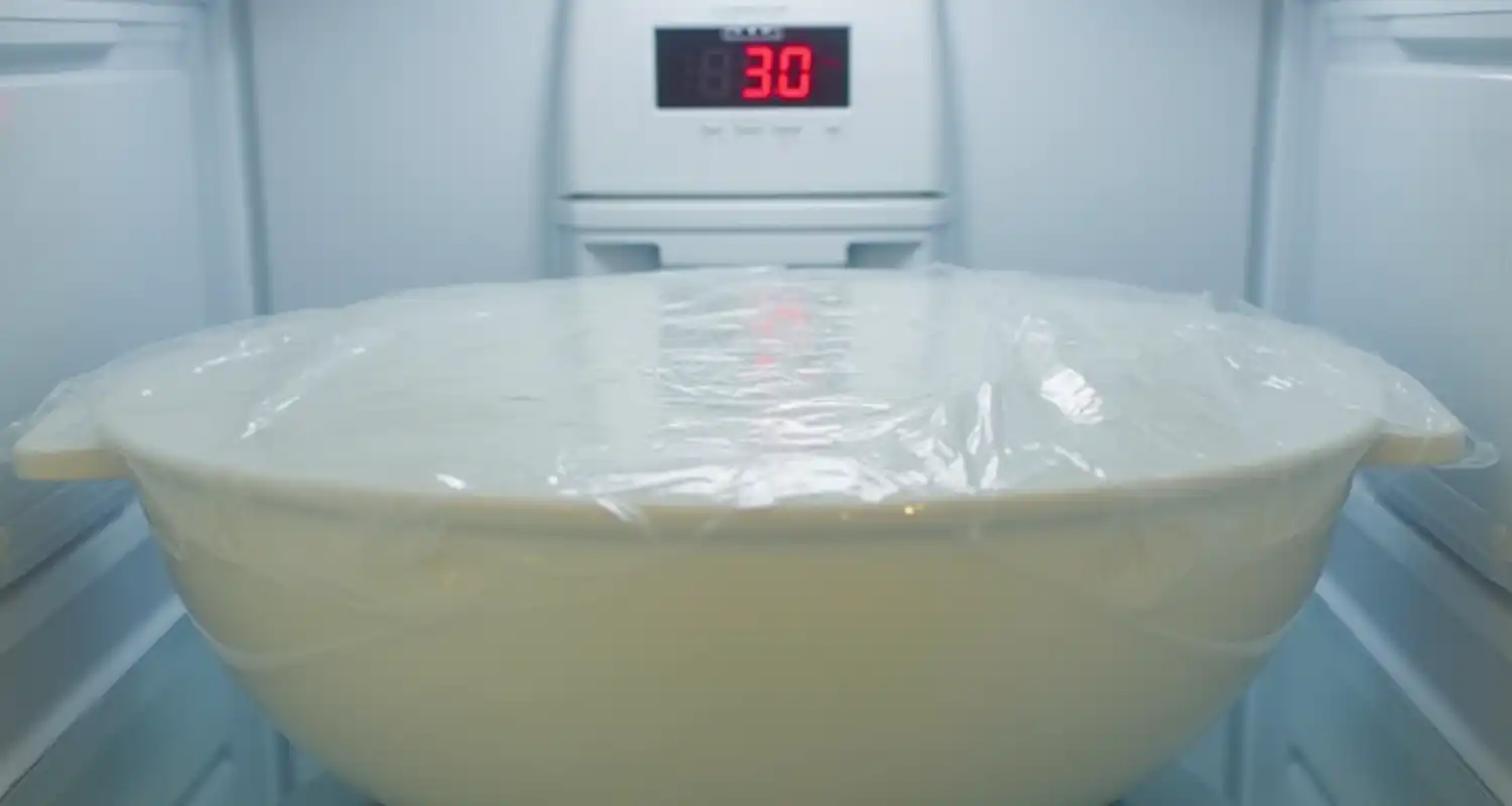 A mixing bowl covered in plastic wrap being chilled in the refrigerator for 30 minutes.